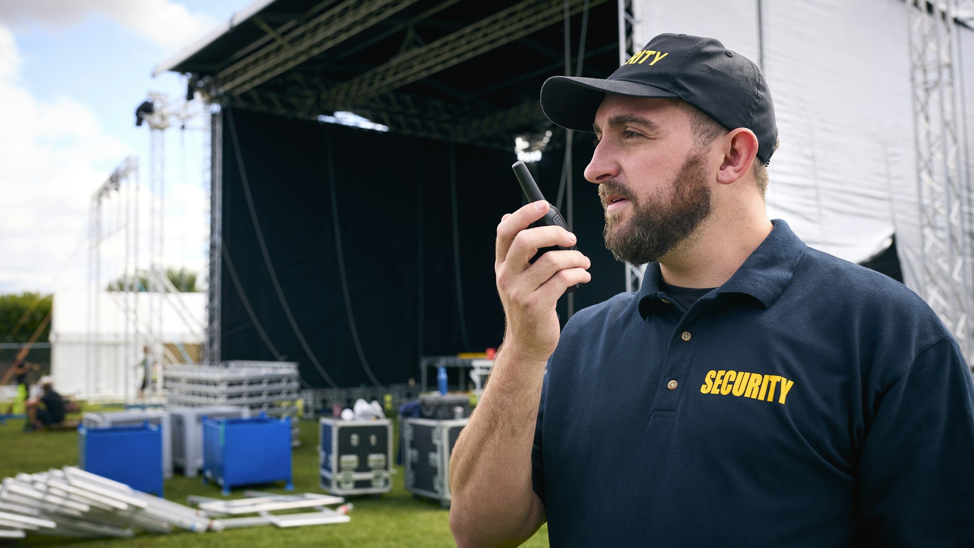 Security Team At Outdoor Stage For Music Festival Or Concert Talking Into Radio